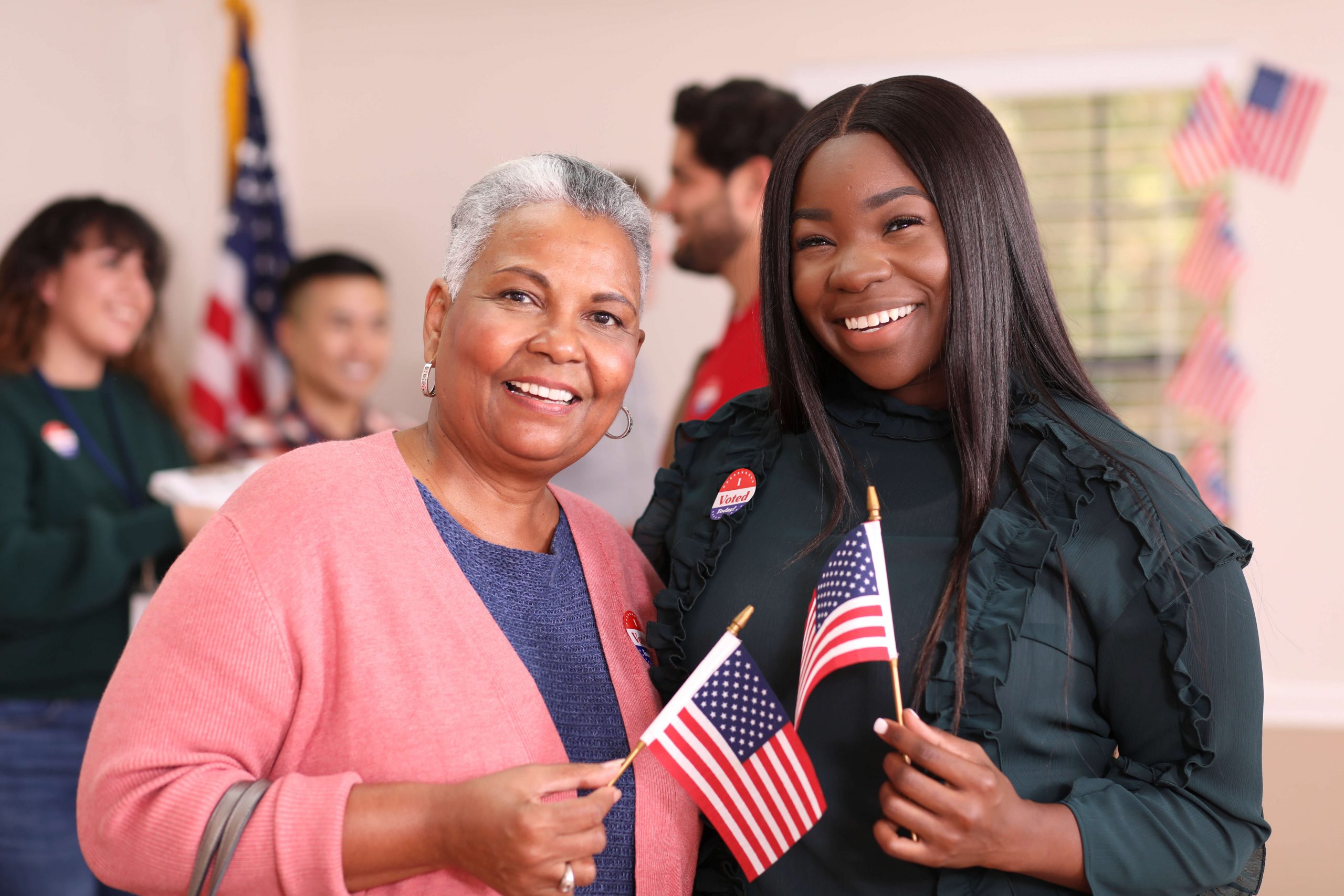Two women at polling place, smiling, holding American flags
